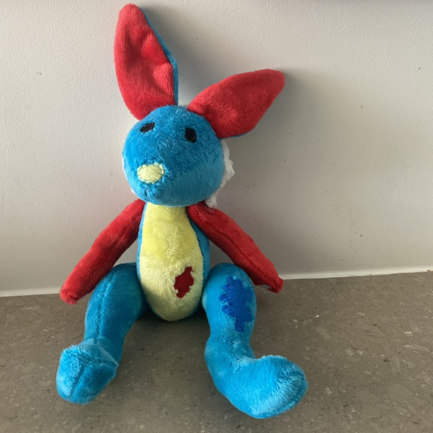 a bright blue hare plush with red ears and arms and a yellow tummy
